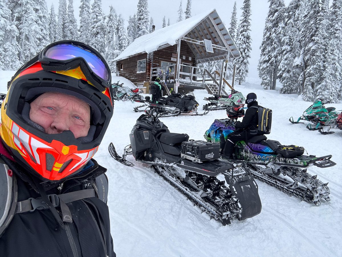 Snowmobiles parked in the snow in front of the Blue Lake cabin, riders gathered between the sleds