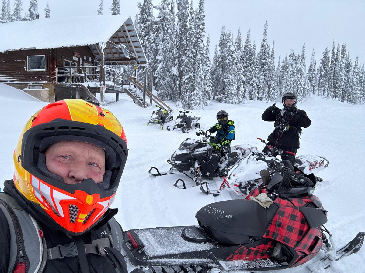Snowmobilers with their sleds in deep snow outside the Blue Lake cabin, snow ghosts behind