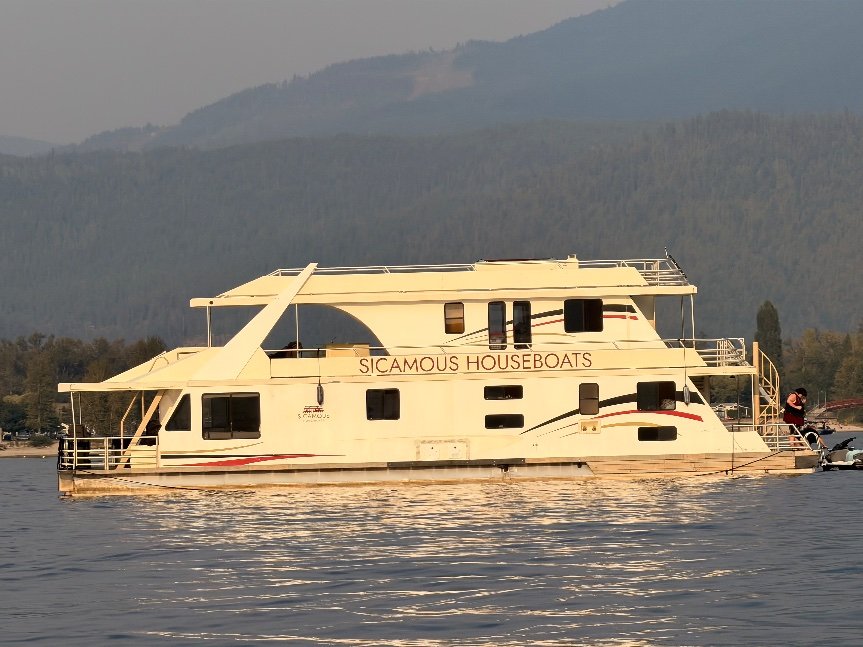 Sicamous Houseboats houseboat anchored on Shuswap Lake with forested mountains behind