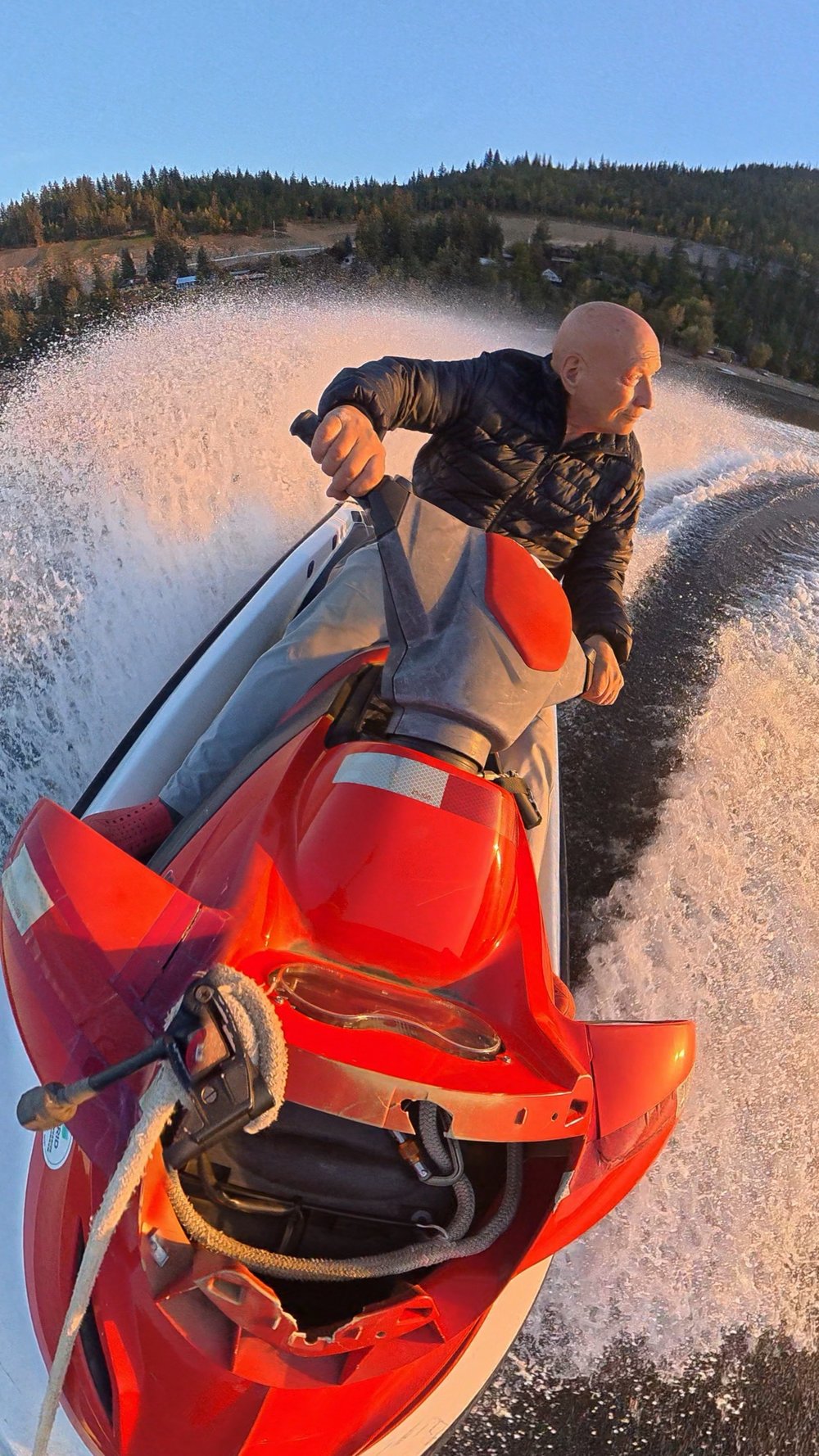 Jet ski heading toward the sunset on Shuswap Lake, spray lit by golden light