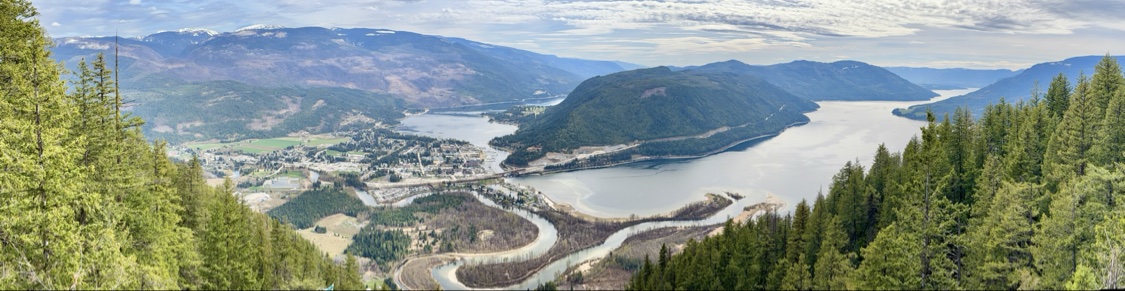 Panoramic view from the mountains over Sicamous town, Shuswap Lake and the winding river, framed by evergreen forest
