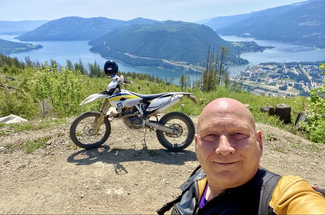 Dirt bike parked at an overlook above town, with Sicamous and Shuswap Lake spread out below between forested mountains