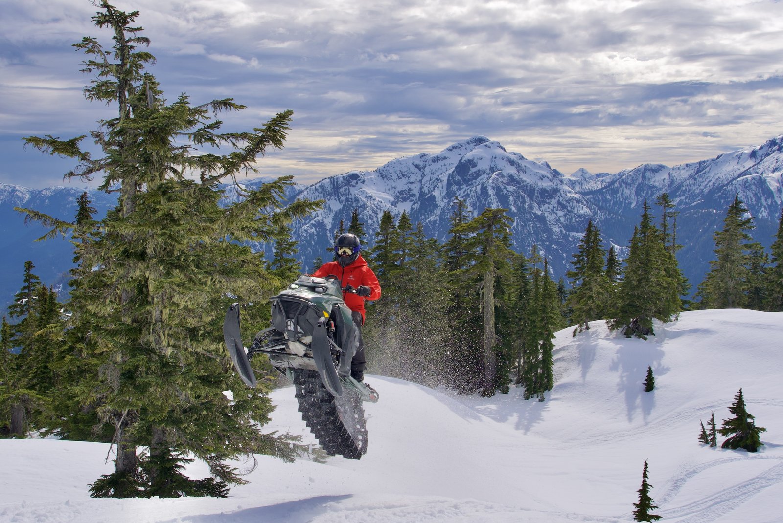 Snowmobile rider catching air against a backdrop of snowy mountains
