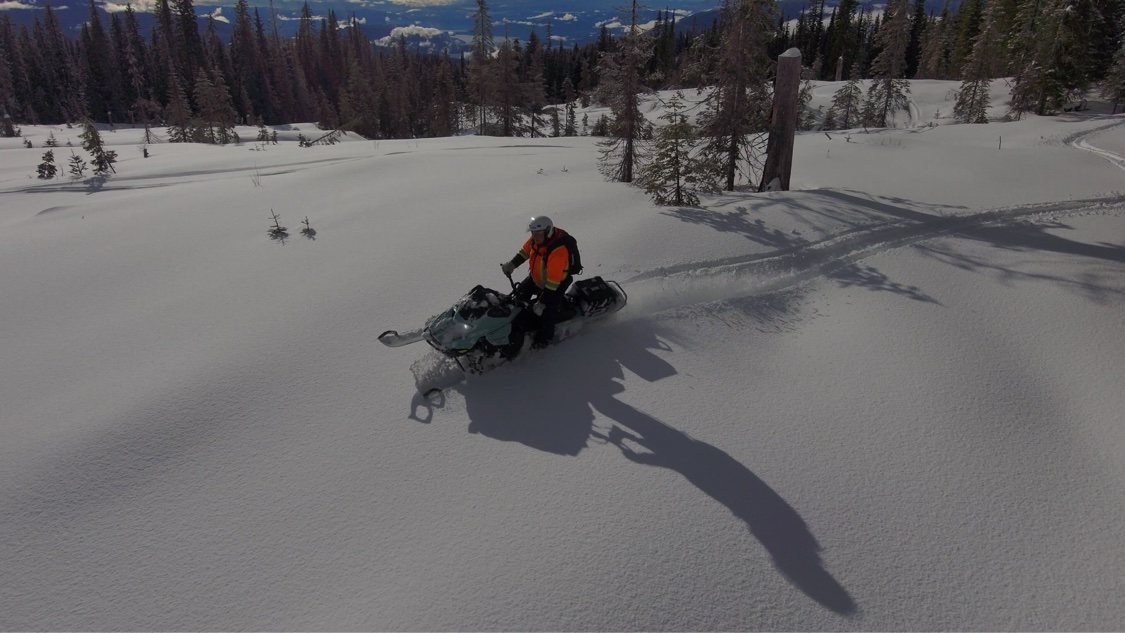 Snowmobile rider carving through deep powder in an open backcountry meadow