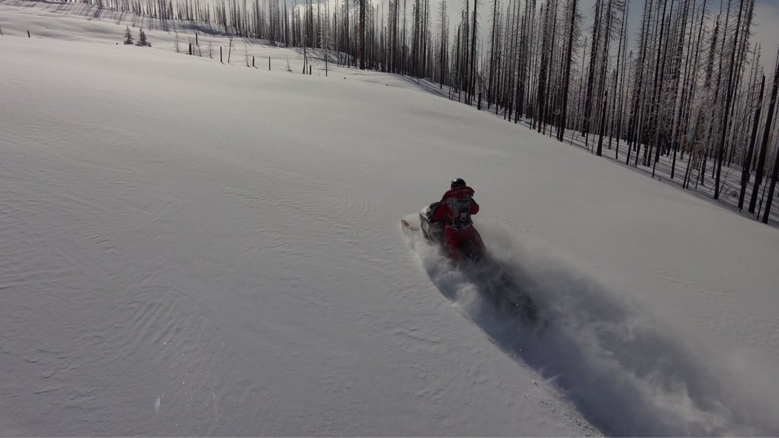Snowmobile rider carving an open snowy slope, powder spraying behind