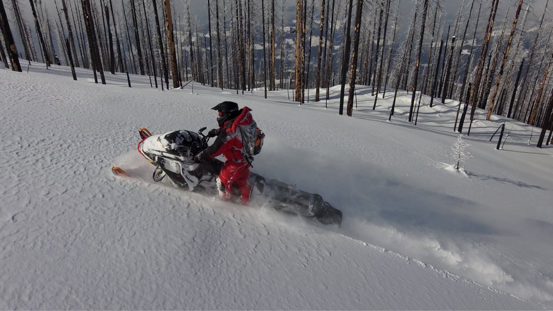 Snowmobile rider carving a turn in deep snow on an open slope