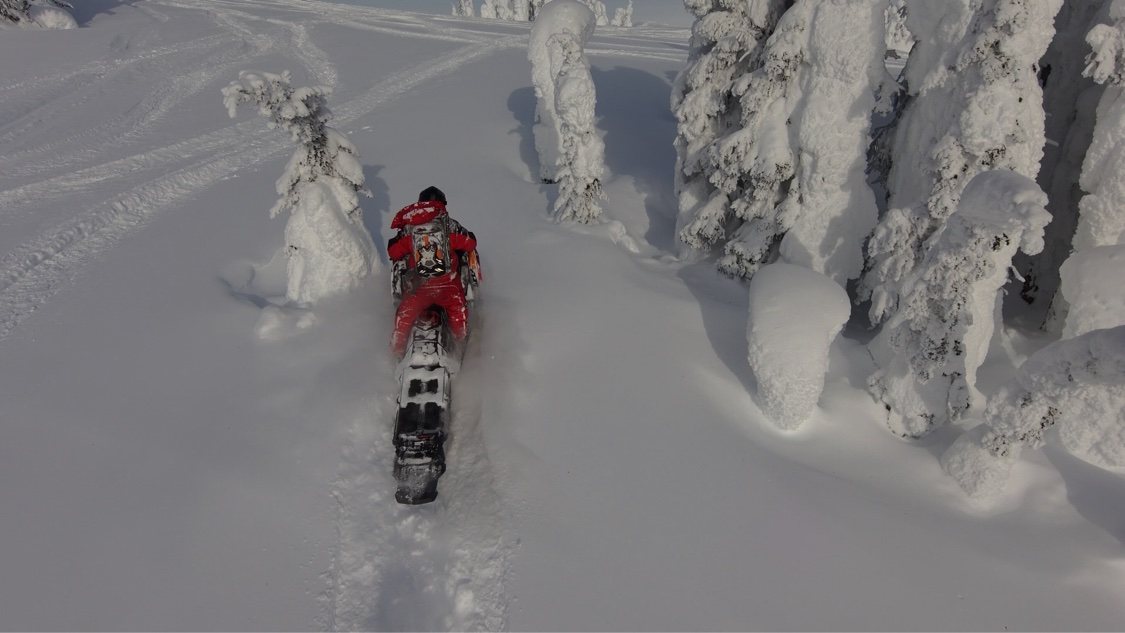 Snowmobile rider threading between snow ghosts on a snowy ridge