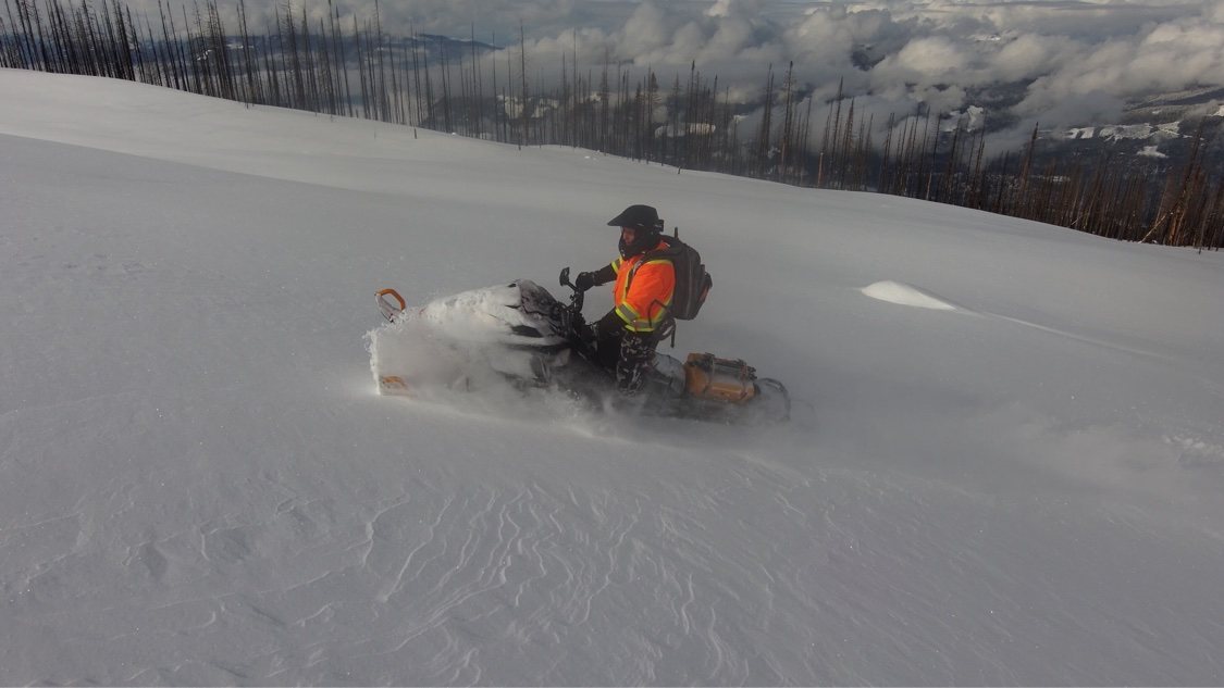 Snowmobile rider carving a high slope above a valley filled with clouds