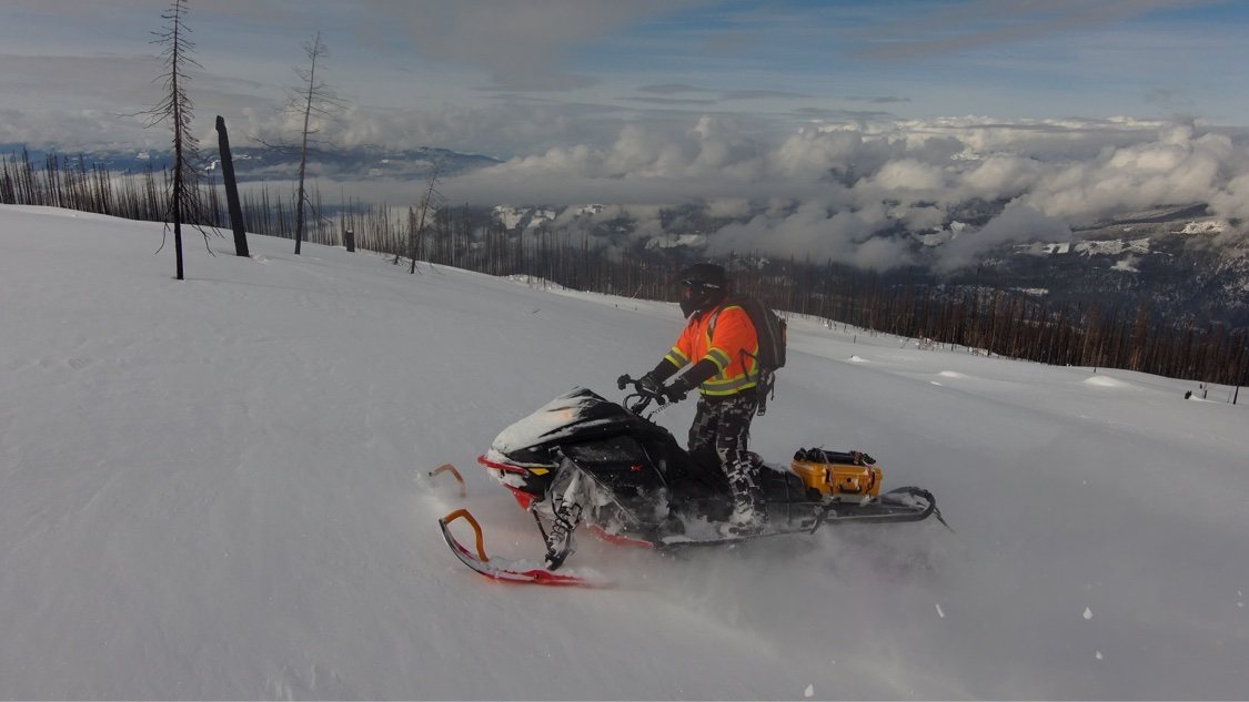 Snowmobile rider on a ridge above a sea of clouds with mountain ranges beyond